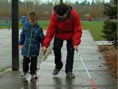 Conner McKittrick showing brother Dalton how to use a white cane in a park