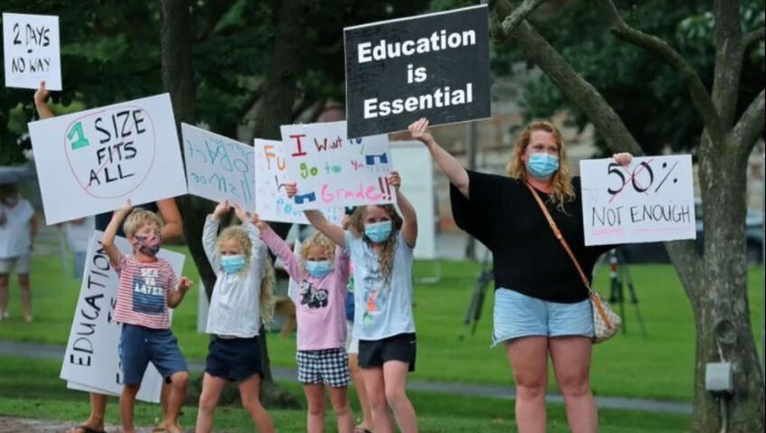 Mother and 4 elementary students protesting remote learning with signs along a street