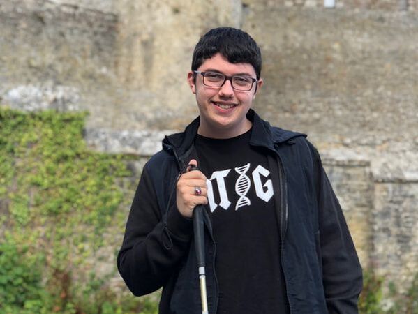 Connor McKittrick smiling with white cane in front of an old castle.