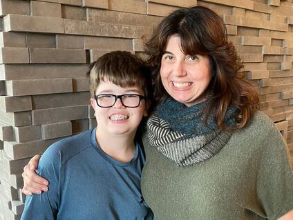 Dr. Lanya McKittrick with son Dalton standing and smiling in front of gray brick wall.