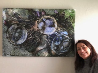 Rose Kamma Morrison, smiling, standing next to an abstract work of art in blues, grays and greens