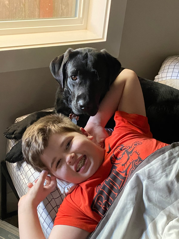 Dalton McKittrick laying on a couch, smiling with a black labrador retriever.